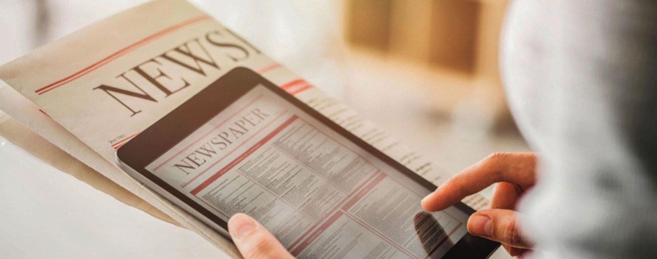 person holding folded newspaper and tablet