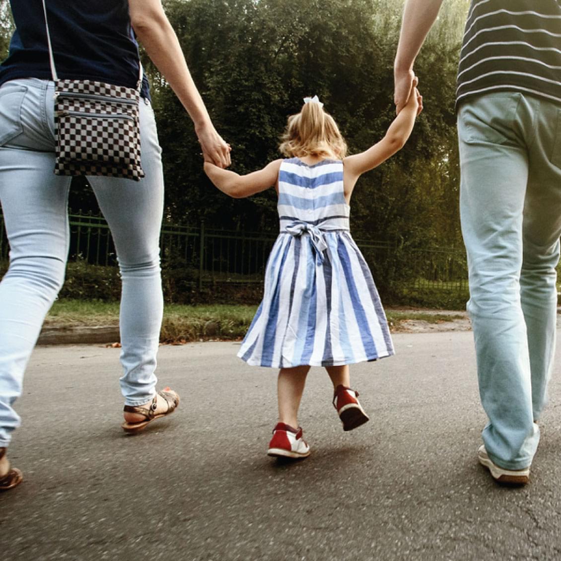 little girl walking with parents, holding their hands