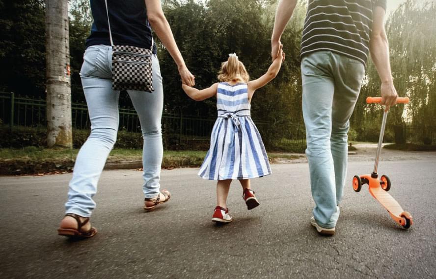 little girl holding her parents' hands, walking on pavement