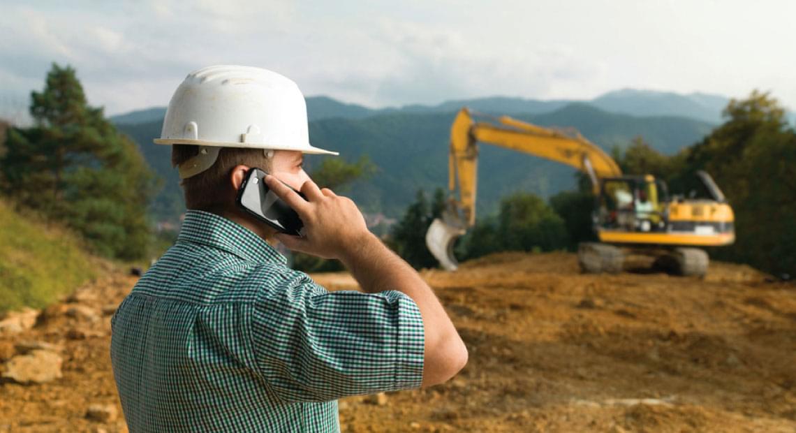 land management worker near construction site talking on cell phone